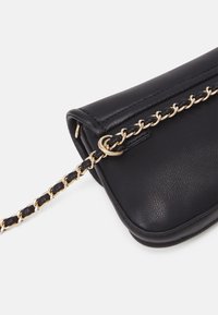 Borsa a tracolla in pelle nera con una catena dorata lucente. Presenta una texture liscia, bordi arrotondati e una chiusura a zip sulla parte superiore.