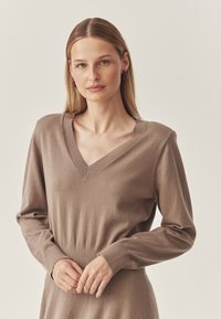 Brūns V veida kakla džemperis ar gariem piedurknēm, ribaina tekstūra un pieguļoša vidukļa daļa. Gluda auduma faktūra un minimālistisks dizains. Smalkas šūšanas detaļas.