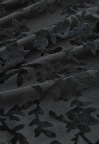 Musta kangas, jossa on teksturoitu kukkakuvio, jossa on kohollaan olevat samettiset lehdet matta taustaa vasten. Sujuva pinta ja pehmeä laskeutuminen.