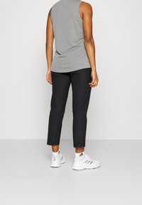 Šedý žebrovaný bezrukávový top, doplněný černými zúženými kalhotami a bílými teniskami. Hladká tkanina s přiléhavým střihem, který zvýrazňuje pas.