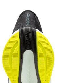 Basket noire avec un dessus texturé, présentant un logo "Reebok" vert, une semelle extérieure en caoutchouc jaune et une semelle intermédiaire blanche avec des accents angulaires.