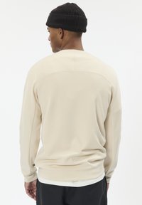 Svetlo béžová mikina s rebrovaným okrúhlym výstrihom a dlhými rukávmi, s hladkou textúrou a prispôsobeným strihom. Minimalistický dizajn bez vzorov.