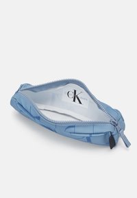 Blå dragkedjefodral med mjukt yttre som har ett enkelt geometriskt mönster. Inuti finns en etikett med texten "Calvin Klein Jeans."
