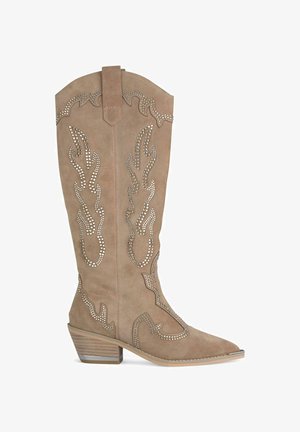 Beige suède cowboyboot met een spitse neus, voorzien van decoratieve vlampatronen en zilveren studs, en een gestapelde hak.