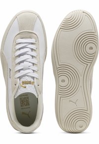 Baskets blanches en cuir lisse et daim doux, dotées d'une semelle texturée avec des motifs circulaires et des accents dorés sur le côté.