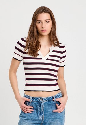Gestreiftes Strickoberteil mit kurzen Ärmeln in Creme, Kastanienbraun und Marineblau. V-Ausschnitt-Design, gerippte Textur und figurbetont an der Taille, kombiniert mit blauen Jeans.