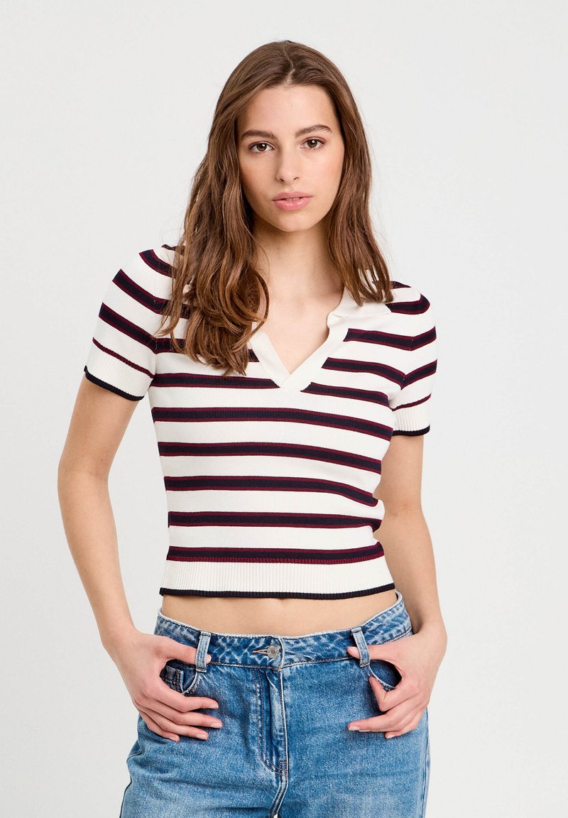 Top en tricot rayé à manches courtes en crème, bordeaux et marine. Design en V, texture côtelée et ajusté à la taille, associé à un jean bleu.