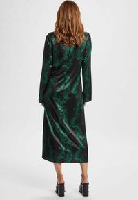 Rochie lungă neagră cu mâneci lungi, decorată cu un model verde spiralat, realizată dintr-un material lucios. Prezintă o croială dreaptă, lungime până la jumătatea gambei și fermoar la spate.