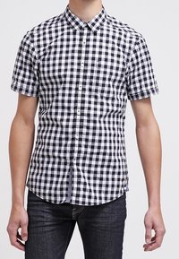 Camisa de manga corta de cuadros con un patrón de gingham en blanco y negro, cuello abotonado y bolsillo en el pecho. Confeccionada en tejido ligero.