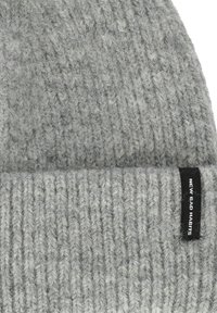 Grijze gebreide beanie met een geribde textuur, voorzien van een zwart label met witte tekst "NEW BAD HABITS" aan de zijkant.