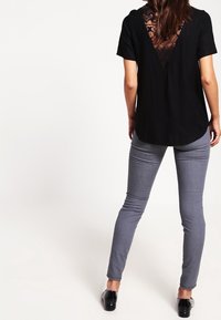 Top negro de manga corta con panel de encaje en la parte posterior, combinado con jeans gris ajustados. El top tiene un dobladillo redondeado y un corte relajado.