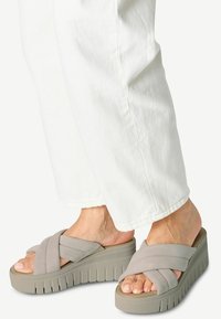 Sandalias de plataforma grises con correas entrecruzadas, que presentan una suela texturizada y una altura moderada, combinadas con pantalones blancos de pierna ancha.