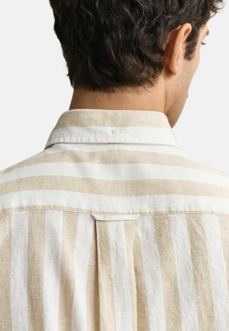 Mann trägt beige-weiß gestreiftes Hemd mit vertikalen Streifen, Ansicht von hinten, zeigt Kragen und obere Rückenpartie.