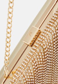 Kopertówka w złotym odcieniu z teksturowaną powierzchnią ozdobioną błyszczącymi kryształkami. Posiada łańcuszkowy pasek i metaliczne zapięcie.