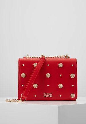 Rød læder Versace Jeans Couture skuldertaske med guldtonede nitter og kæderem, vist på hvid piedestal mod ensfarvet baggrund.