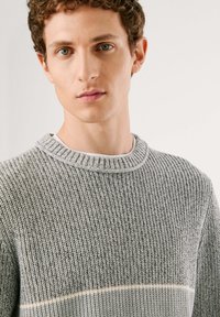 Grauer Strickpullover mit rundem Halsausschnitt und strukturiertem Stoff, der ein dezentes horizontales Streifenmuster über der Brust aufweist.