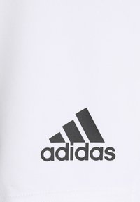 Maglietta sportiva bianca con logo Adidas nero. Presenta un tessuto liscio e traspirante e un design classico a girocollo. Aspetto semplice e moderno.