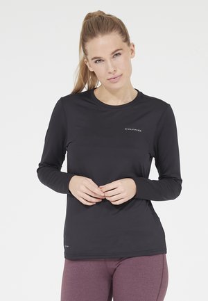 Chemise de sport noire à manches longues avec un col rond et un design ajusté, fabriquée en material lisse et extensible. Logo affiché sur la poitrine.