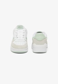 Zapatillas Lacoste con parte superior de cuero blanco, detalles en gamuza de color gris claro y una lengüeta en verde menta en el talón. Cintas planas y diseño de puntera perforada.