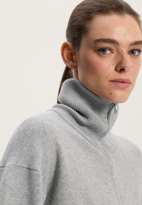 Gray sweater with a high ribbed collar and a half zipper, featuring a soft texture and relaxed fit. Smooth fabric with subtle detailing.