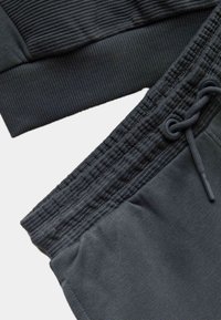 Ropa deportiva de color gris oscuro con textura acanalada en los puños del sudadera y un acabado liso en los pantalones de chándal con cordón ajustable.