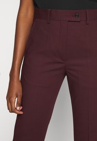Bordowe spodnie typu tapered z płaskim przodem, paskami na pasek i pojedynczym zapięciem na guzik. Posiadają gładką fakturę i dopasowany krój.