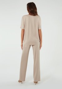 Beżowy dwuczęściowy zestaw składający się z luźnej bluzki z krótkim rękawem i spodni z szerokimi nogawkami, wykonany z gładkiego materiału z minimalnymi detalami.