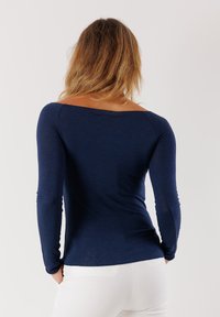 Maglietta a maniche lunghe blu navy con scollatura rotonda, design aderente e texture morbida, abbinata a pantaloni bianchi. Vista dal retro.