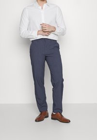 Witte langetermijnsleeve shirt gecombineerd met marineblauwe pantalon en bruine leren schoenen. De stof lijkt glad met een klassieke pasvorm.