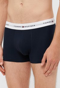 Sötétkék pamut boxer alsó fehér elasztikus derékkal, amelyen ismétlődő logó mintázat található. Testhez simuló fazon, sima textúrával és varrásokkal.