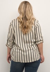 Beige overhemd met zwarte verticale strepen, opgerolde mouwen, achteraanzicht. Gecombineerd met donkerblauwe jeans, gestructureerde stof, getailleerde pasvorm.