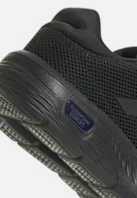 Chaussure de sport noire dotée d'un supérieur en mesh respirant, d'une semelle rembourrée et d'une étiquette "Cloudfoam Comfort" visible. Semelle extérieure en caoutchouc texturé avec des rainures.