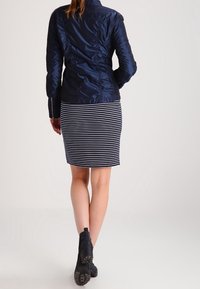 Navy blue, textured jacket with a fitted design, paired with a striped pencil skirt. Black ankle boots complete the outfit.