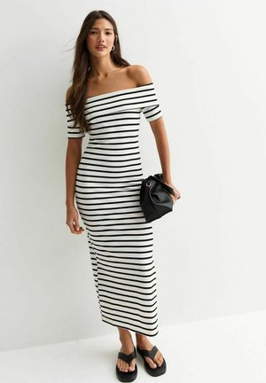 Vestido maxi de rayas en blanco y negro, de hombros caídos, con silueta ajustada, combinado con un bolso negro y sandalias planas.