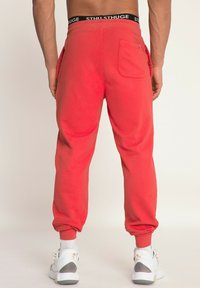 Rode joggingbroek van zacht katoen, met een elastische tailleband met zwarte letters, omgeslagen enkels en een achterzak.