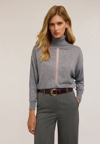 Šedý rolák s průhledným panelem; volný střih. V kombinaci se šedými pruhovanými kalhotami a vínovým koženým opaskem se zlatým kováním.