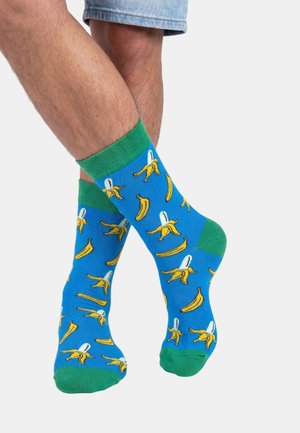 Beneden gekruist met blauwe sokken met groene boord en tenen, bedrukt met geschilde en hele gele bananen.
