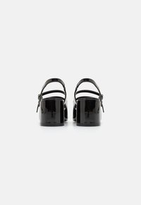 Sandali con tacco in pelle verniciata nera, dotati di cinturini regolabili, tacchi a blocco e una finitura liscia, che mettono in evidenza un design minimalista.