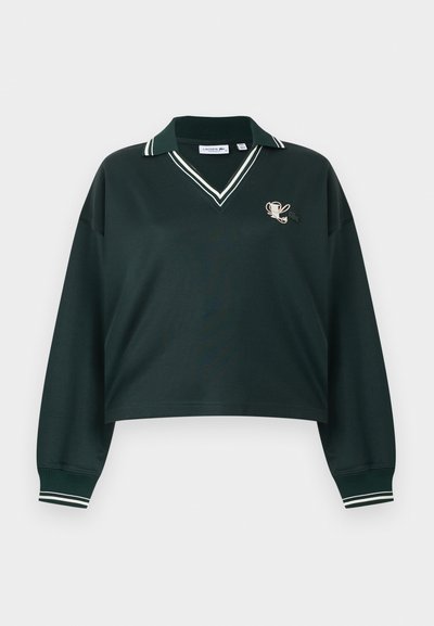 Polo manches longues vert foncé avec col et poignets à rayures blanches, col en V, et petit trophée et trèfle brodés sur la poitrine.