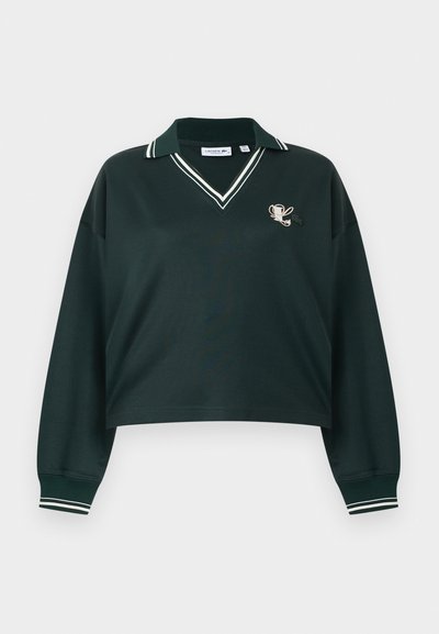 Polo manches longues vert foncé avec col et poignets à rayures blanches, col en V, et petit trophée et trèfle brodés sur la poitrine.