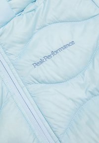 Giacca isolante blu chiaro con design trapuntato, texture liscia e zip, logo "PeakPerformance" in rilievo con filo abbinato.