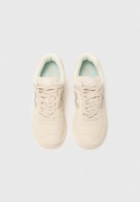 Pair of beige New Balance sneakers with laces, viewed from above on a white background.