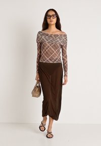 Hosszú ujjas, vállról lelógó blúz kockás mintával, amelyet egy barna, elegáns maxiszoknyával párosítanak. Kényelmes szandál és egy kicsi kézitáska kíséretében viselik.