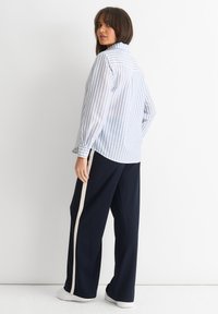 Striped button-up shirt in light blue and white with a relaxed fit; paired with navy wide-leg pants featuring a cream side stripe.
