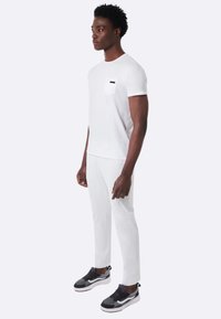 Maglietta bianca a maniche corte con taschino sul petto, abbinata a pantaloni bianchi e scarpe da ginnastica nere. Design semplice e pulito.