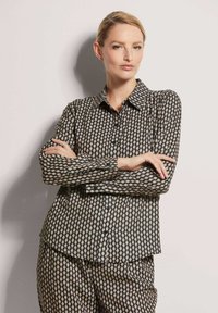 Schwarz-weiße gemusterte Hemd mit Kragen, langen Ärmeln und Rautenmuster, kombiniert mit passenden Hosen. Glatte Stofftextur.