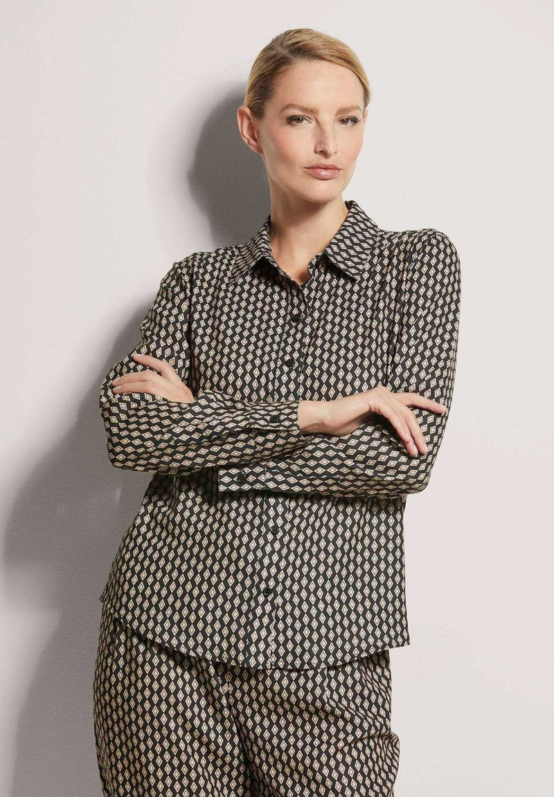 Schwarz-weiße gemusterte Hemd mit Kragen, langen Ärmeln und Rautenmuster, kombiniert mit passenden Hosen. Glatte Stofftextur.