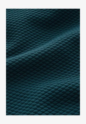 Tirkizna teksturirana tkanina s dijamantnim uzorkom, sa mekanom, rebrastom površinom koja stvara dubinu i vizualni interes.