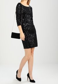 Svart paljettklänning med trekvartsärmar, figursydd form och rund halsringning. Kommer med svarta högklackade skor och en liten svart handväska.