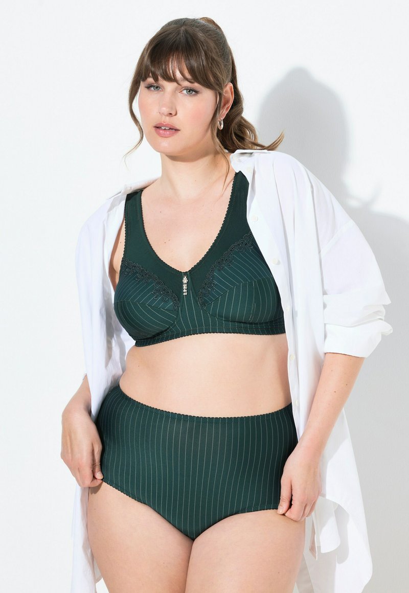 Donkergroen gestreept bh en hoogstaand slipset, met kantaccenten en een klein decoratief element in het midden. Draagt met een open witte blouse.